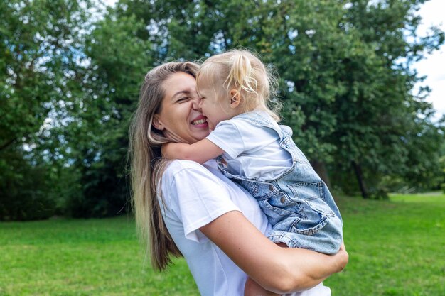 Een moeder met een kleine dochter in haar armen lacht en knuffelt in een zomerpark liefde en tederheid