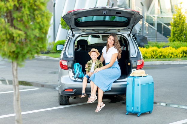 Een moeder met een zoontje in de auto en een blauwe koffer gaan op vakantie of op reis voor de luchthaven