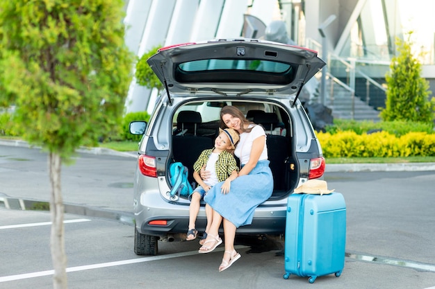 Een moeder met een zoontje in de auto en een blauwe koffer gaan op vakantie of op reis voor de luchthaven
