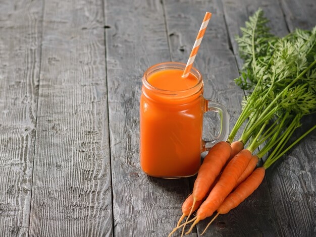 Een mok verse wortel smoothie met een cocktail buis op een donkere houten tafel.