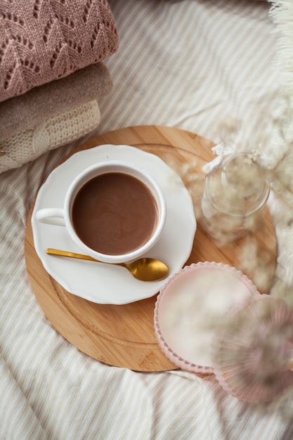 Een mok warme chocolademelk, gebreide truien, een boeket witte gedroogde bloemen in een vaas, een kaars op het bed. Ontbijt op bed. Knus. De lente.