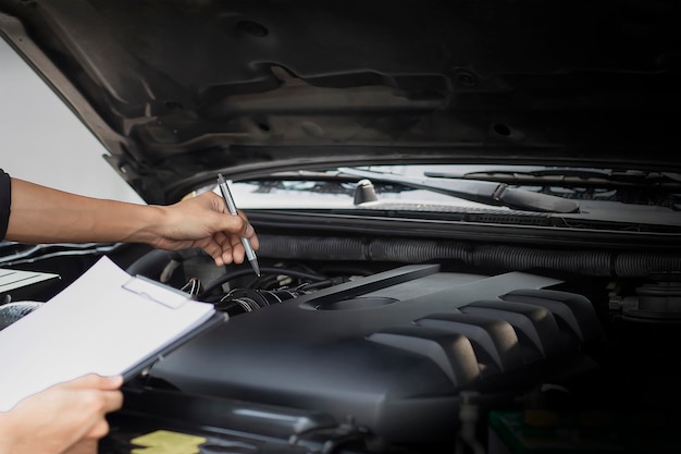 Een monteur schrijft op een klembord naast de motor van een auto.