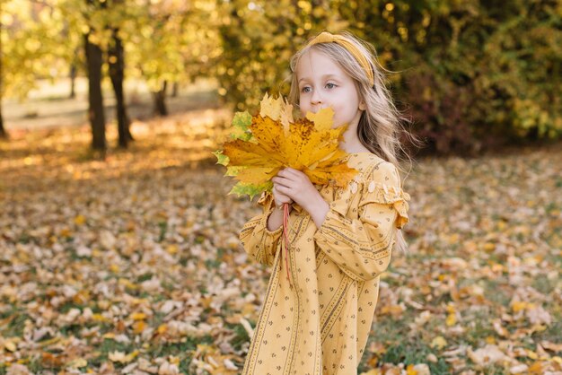 Een mooi blond meisje loopt in een herfstpark met gele esdoornbladeren