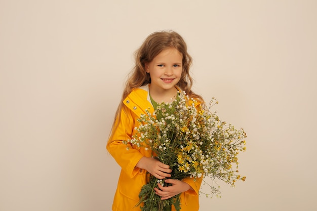 een mooi blond meisje met blauwe ogen een gele regenjas houdt wilde bloemen in haar handen