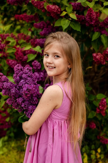 Een mooi blond meisje met lang haar heeft een boeket seringen in haar handen