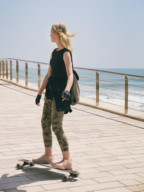 Een mooi blond meisje op skateboard in warme zomerdag aan de kust