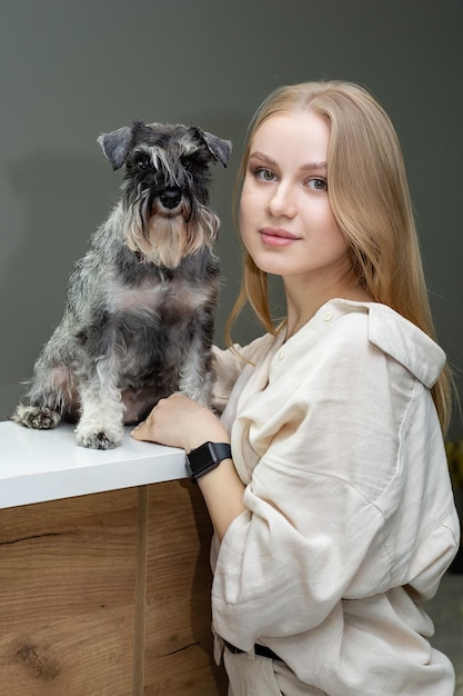 een mooi blond meisje staat bij de receptie waarop een miniatuur Schnauzer-hond zit