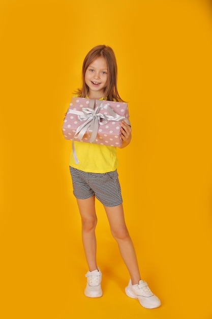 een mooi bruinharig meisje in een geel T-shirt houdt een geschenkdoos in haar handen gele achtergrond