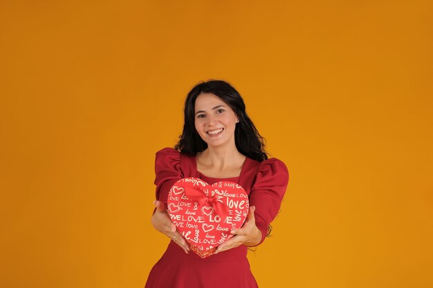 een mooi brunette meisje in een rode jurk heeft een hartvormige geschenkdoos in haar handen