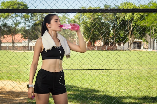 Een mooi fitness meisje drinkwater uit een roze fles terwijl ze luistert naar muziek op haar koptelefoon