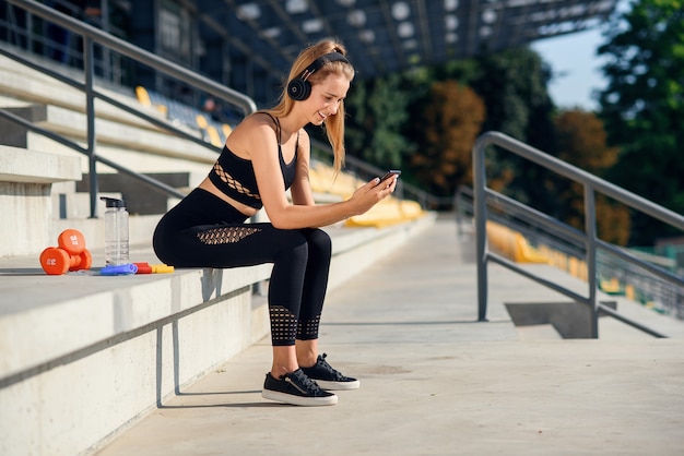 Een mooi fitnessmeisje in grijze sportkleding gebruikt een smartphone en luistert na het sporten naar muziek in het stadion. sport en gezond concept.