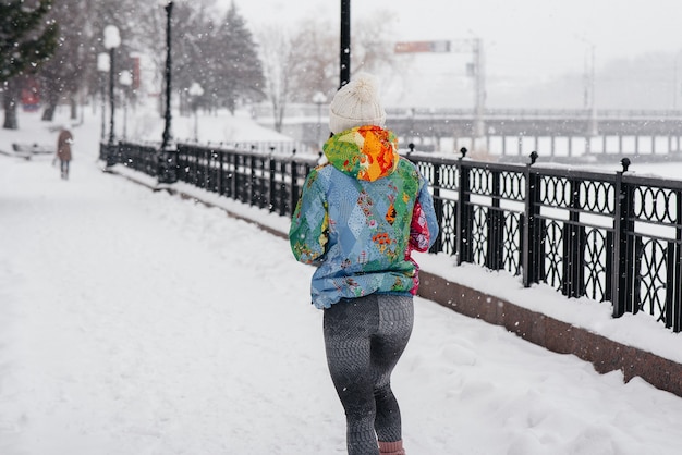 Een mooi jong meisje jogt op een ijzige en besneeuwde dag. Sport, gezonde levensstijl.