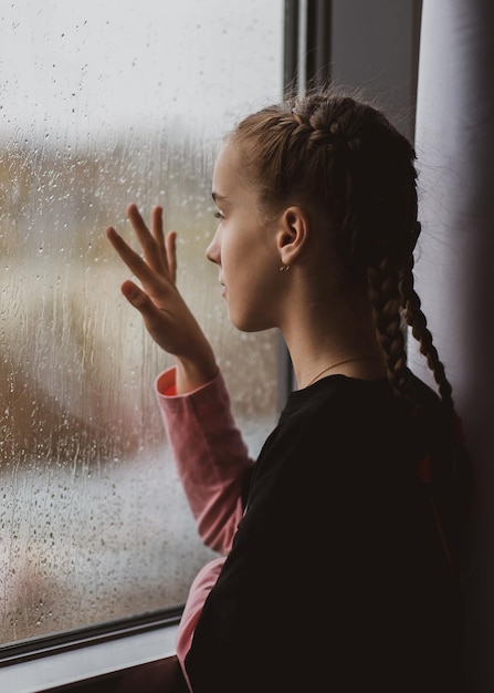 Een mooi jong meisje kijkt uit het raam met regen en dromen Regen Herfst Sfeer