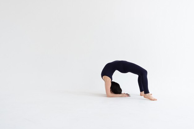 een mooi jong meisje met donker haar staat in de Urdhva Dhanurasana pose op een witte achtergrond