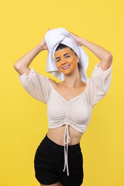 Een mooi jong meisje met een scrubmasker op haar gezicht poseert voor de camera en glimlacht tegen een gele achtergrond