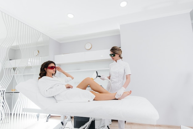 Een mooi jong meisje zal laserontharing ondergaan met moderne apparatuur in een spa-salon. schoonheidssalon. lichaamsverzorging.