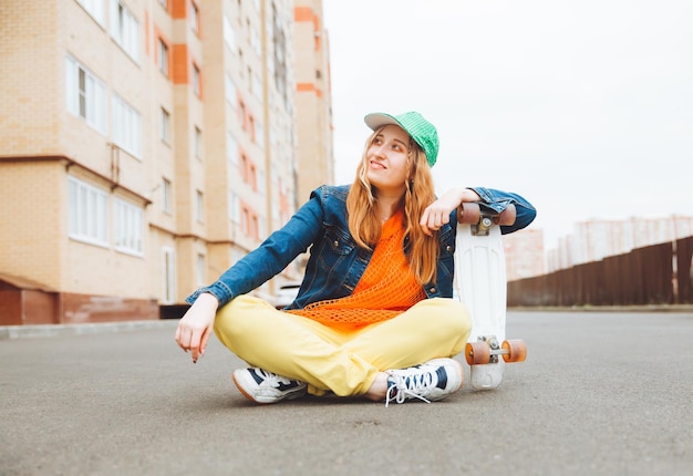Foto een mooi jong tienermeisje zit op de grond met een schaats bij zonnig weer generatie z