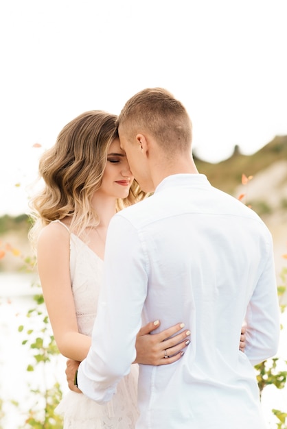 Een mooi jong verliefd stel, een man en een vrouw omhelzen, kussen in de buurt van een blauw meer en zand bij zonsondergang. Vakantie aan zee op het strand