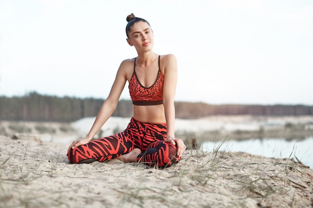 Een mooi Kaukasisch meisje in een heldere rode sportkleding doet yogapositie het uitrekken zich op aard