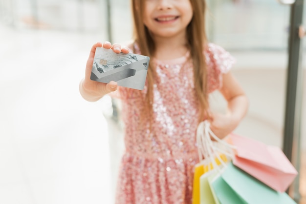 Een mooi kind in het winkelcentrum maakt winkelen. Online winkelen concept. Een meisje in een roze jurk met veelkleurige pasteltassen in haar handen