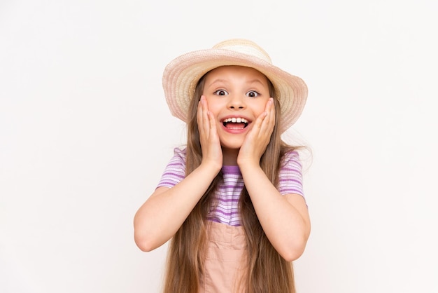 Een mooi klein meisje houdt haar wangen vast en glimlacht breed Een kind met een hoed op een witte geïsoleerde achtergrond