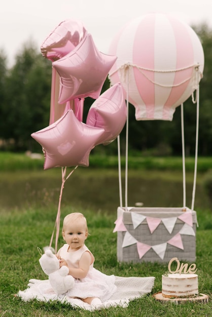 Een mooi klein meisje in een mand met een ballon en een taart viert haar eerste verjaardag