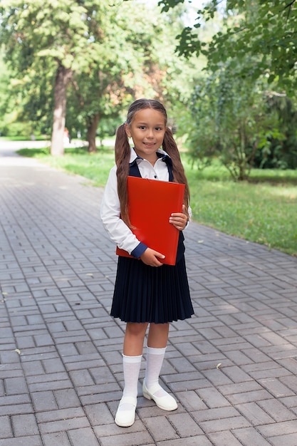 Een mooi klein schoolmeisje met een roze rugzak loopt in het park, het concept om terug te keren naar school. Schooluniform