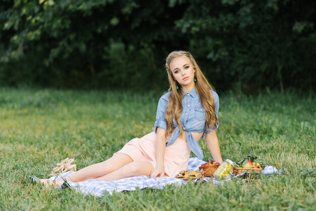 Een mooi lief meisje in een blauw denim shirt en een chiffon roze rok zit op een plaid op een zomerpicknick