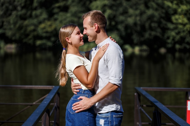 Een mooi liefdevol jong stel staat aan de oever van de rivier die ze knuffelen. Gelukkig getrouwd stel op vakantie aan het meer