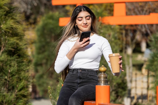 Een mooi meisje dat haar koffie vasthoudt en met haar telefoon speelt Foto van hoge kwaliteit