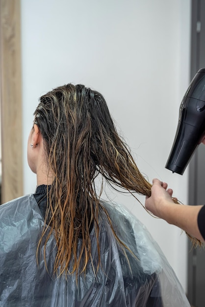 Een mooi meisje dat voor het eerst naar de schoonheidssalon kwam, heeft haar haar gebleekt en gedroogd om verf aan te brengen Haardroogconcept Schoonheidssalonconcept