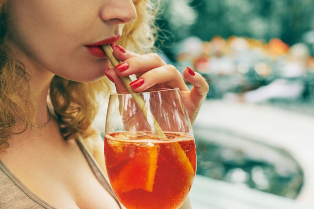 Een mooi meisje drinkt via een eco-buisje een aperol spritz alcoholische cocktail met ijs.