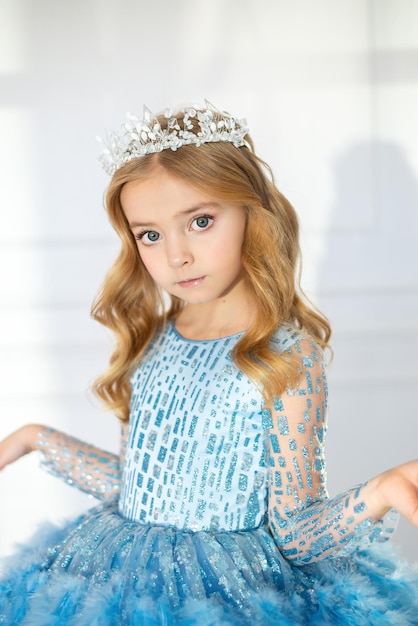 Foto een mooi meisje in een blauwe jurk. kindermake-up en kapsel voor een kleine prinses, haarversieringen