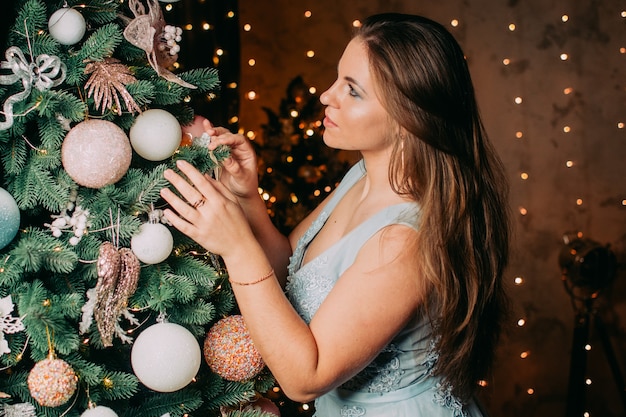 Een mooi meisje in een blauwe jurk versiert een kerstboom Nieuwjaarsconcept