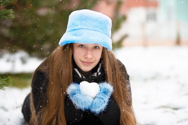 Foto een mooi meisje in een bontmuts en wanten houdt een sneeuwbal in haar handen