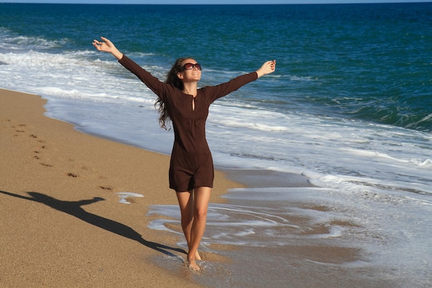 Een mooi meisje in een bruine jurk loopt over het zandstrand en geniet van het uitzicht op zee