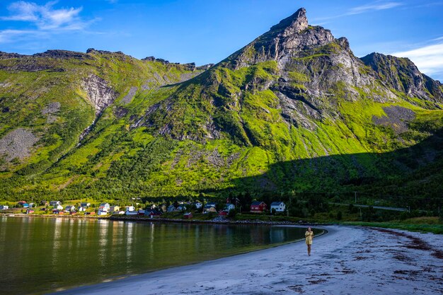 een mooi meisje in een gele jurk loopt op een strand omringd door machtige bergen, senja, noorwegen