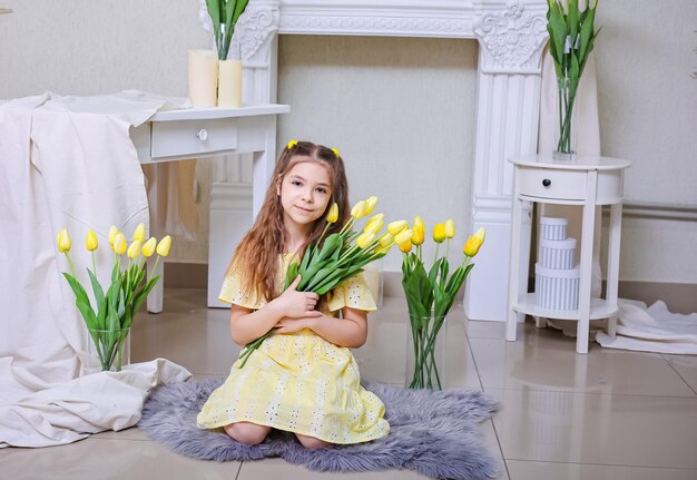 Een mooi meisje in een gele jurk tegen de achtergrond van boeketten gele tulpen