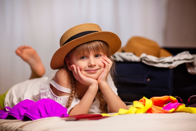 Een mooi meisje in een hoed klaar voor vakantie ligt glimlach op het bed een strandreis naar de zee bereidt bagage opheffing van beperkingen voor toeristen voor