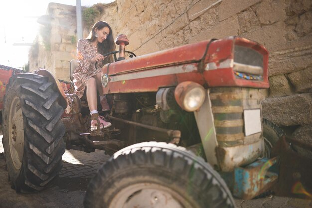 Een mooi meisje in een jurk rijdt op een oude tractor