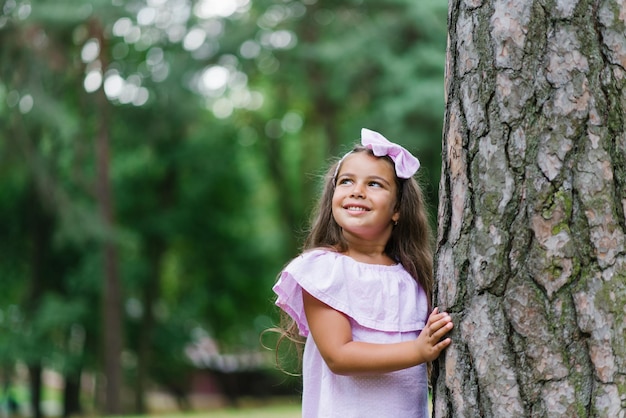 Een mooi meisje in een roze jurk staat in de zomer bij een boom in het bos te glimlachen en te dromen