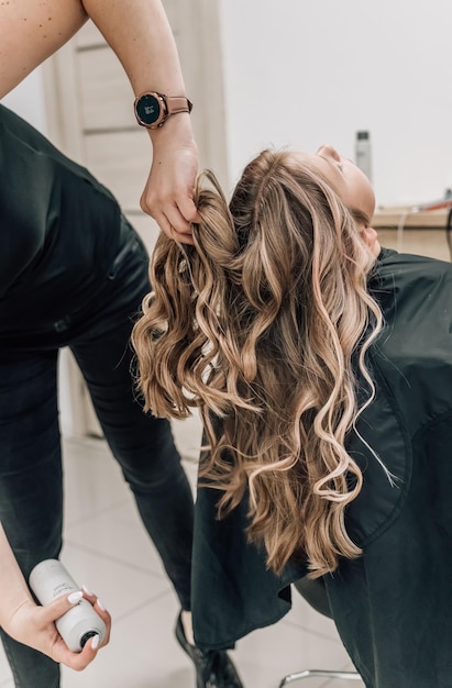 Een mooi meisje in een schoonheidssalon maakt een chique kapsel Sprays met haarlak