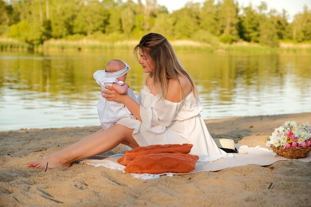 Een mooi meisje in een witte jurk met een pasgeboren baby zit op het strand op het zand