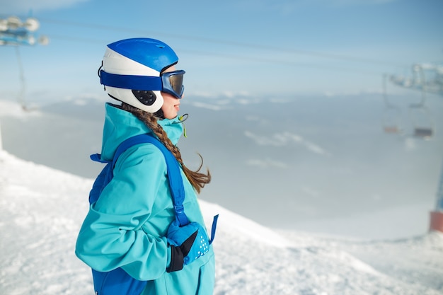 Een mooi meisje in winterkleren, een blauwe helm en een groen jasje vermaakt zich prima in de bergen.