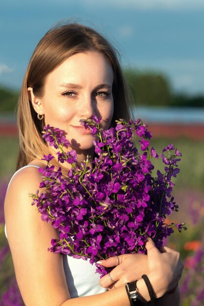 een mooi meisje met blond haar heeft een boeket fel lila veldbloemen in haar handen