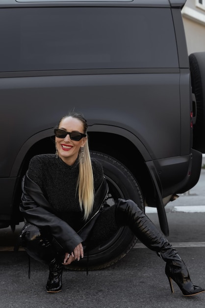 Een mooi meisje met blond haar met een grote zwarte auto in een jurk met open rug. Lang haar en