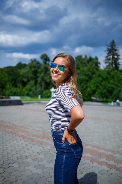 Een mooi meisje met blond lang haar van Europese uitstraling. Gekleed in jeans en een T-shirt. Loop op een zonnige dag