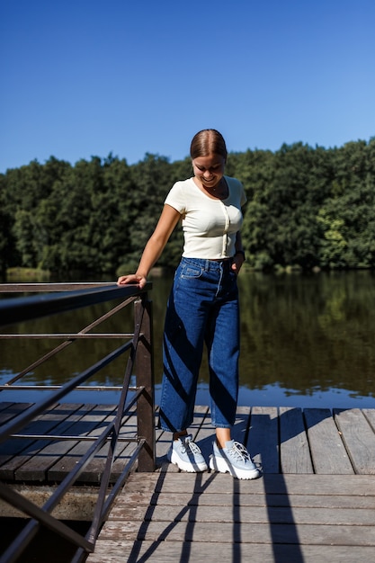 Een mooi meisje met een Europese uitstraling. Een jonge vrouw loopt langs de rivier. Gekleed in jeans en een T-shirt.