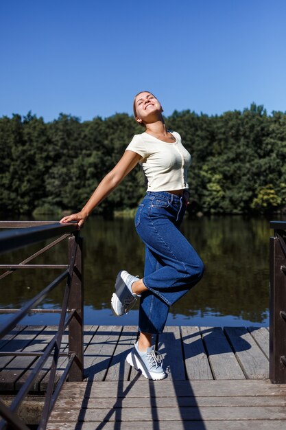 Een mooi meisje met een Europese uitstraling. Een jonge vrouw loopt langs de rivier. Gekleed in jeans en een T-shirt.