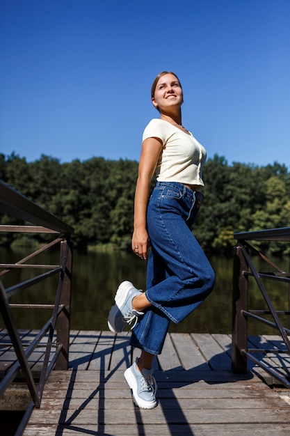 Een mooi meisje met een Europese uitstraling. Een jonge vrouw loopt langs de rivier. Gekleed in jeans en een T-shirt.